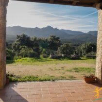Covered veranda with terracotta tiles and granite columns, looking out over a wide, natural landscape and majestic mountain ridge.