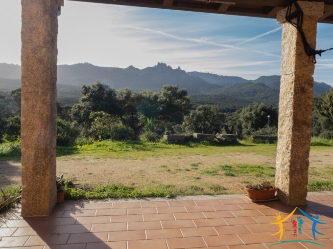 Covered veranda with terracotta tiles and granite columns, looking out over a wide, natural landscape and majestic mountain ridge.